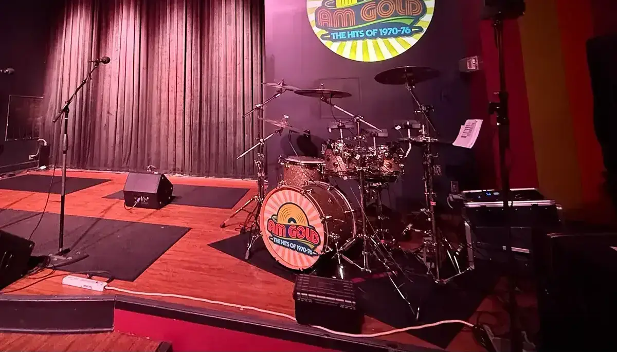 Retro sunburst band logo projected on a club stage wall above the drum kit with a single-lens logo projector