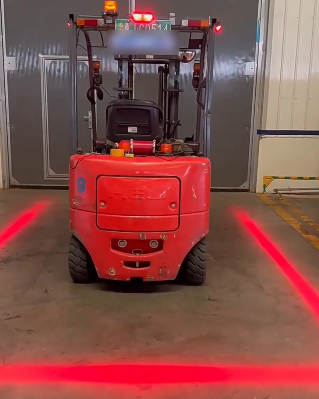Forklift seen from behind with three red boundary lines projected on the warehouse floor