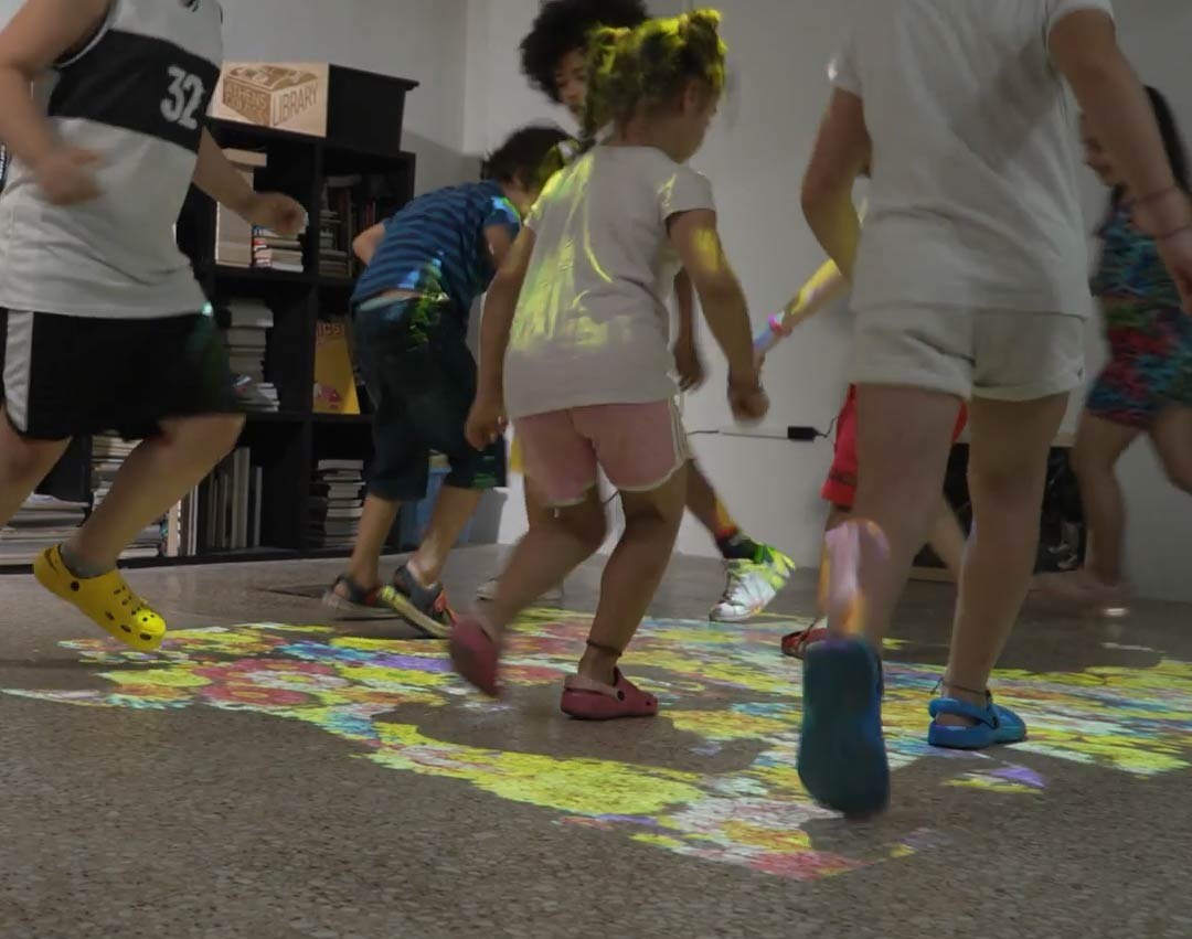 Video: children run across a colorful flower-mosaic game projected on a playroom floor