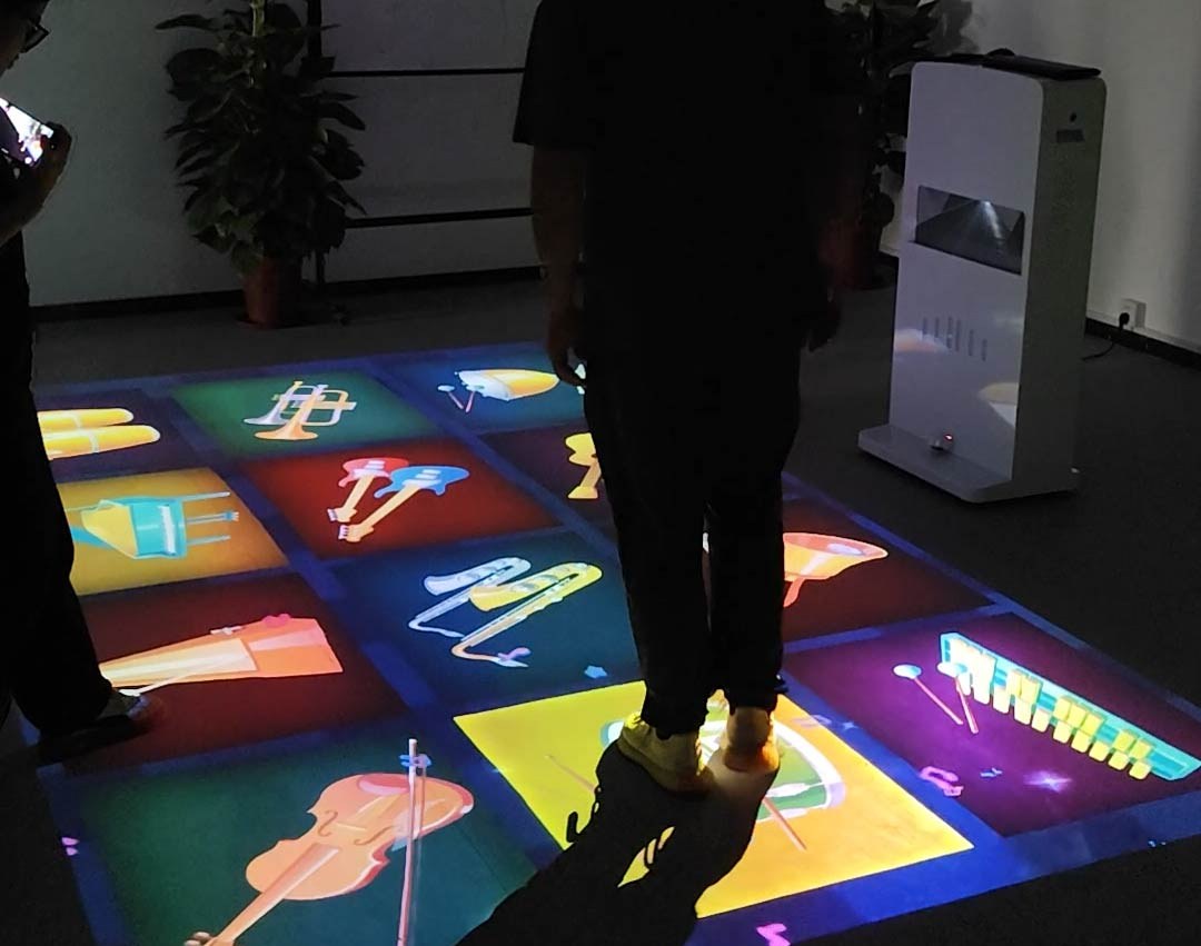Video: player steps on glowing musical instrument panels projected on the floor, triggering sounds in a dark studio