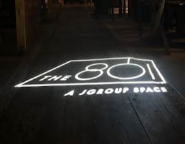 Video: white line-art venue logo gobo projected across dark wood flooring at an event space