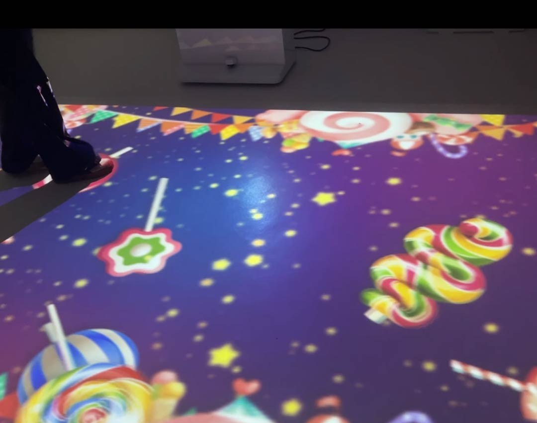 Video: candy-land floor game with lollipops and starry purple sky projected in a bright playroom as a child steps in
