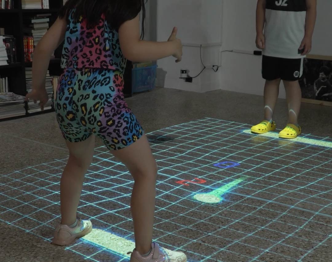 Video: two kids play a glowing grid air-hockey game projected on the floor