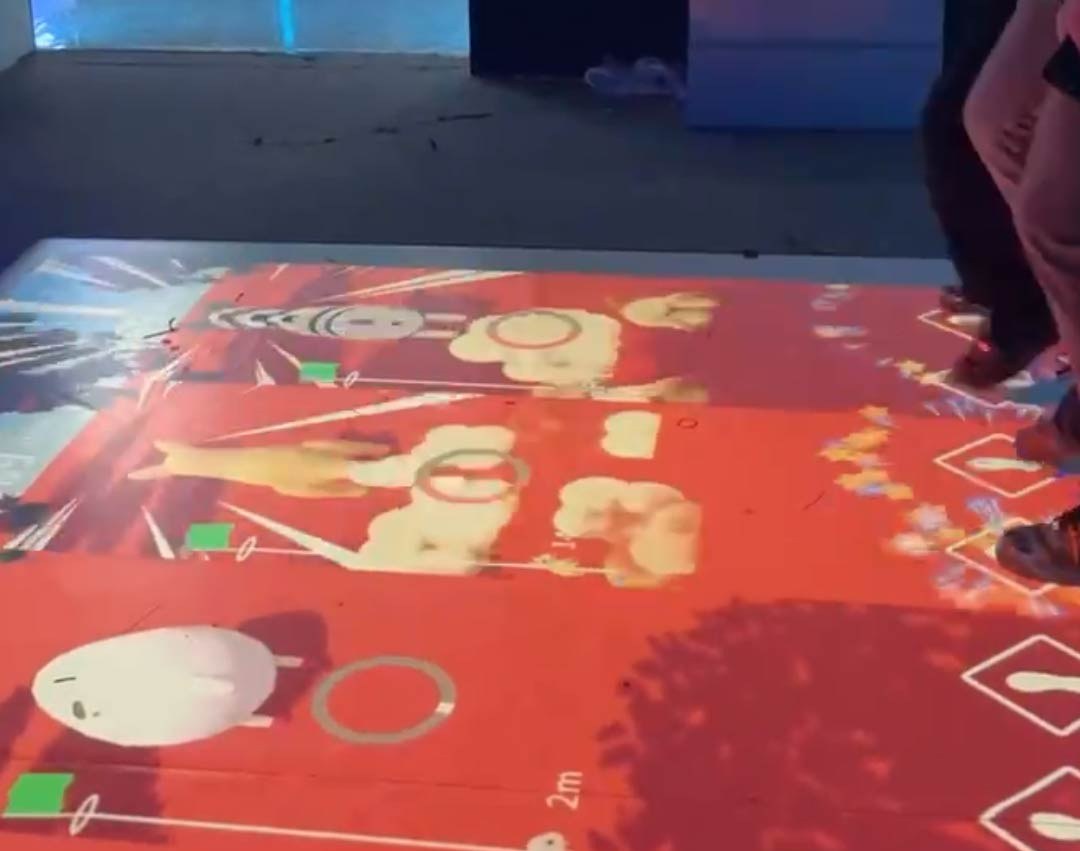 Video: guests play a cartoon target game on a red board projected across an exhibit floor