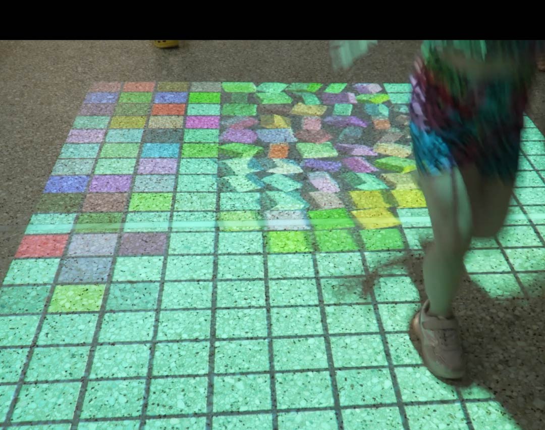 Video: child dashes over a color-tile mosaic grid lighting up an interactive floor