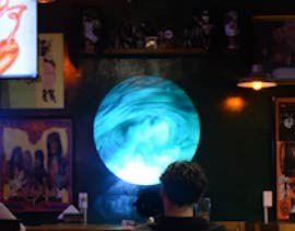 Video: glowing turquoise moon orb projected on a pub wall above seated guests