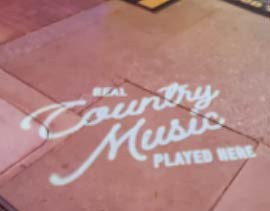 Video: white script sign about live country music projected across brick patio pavers