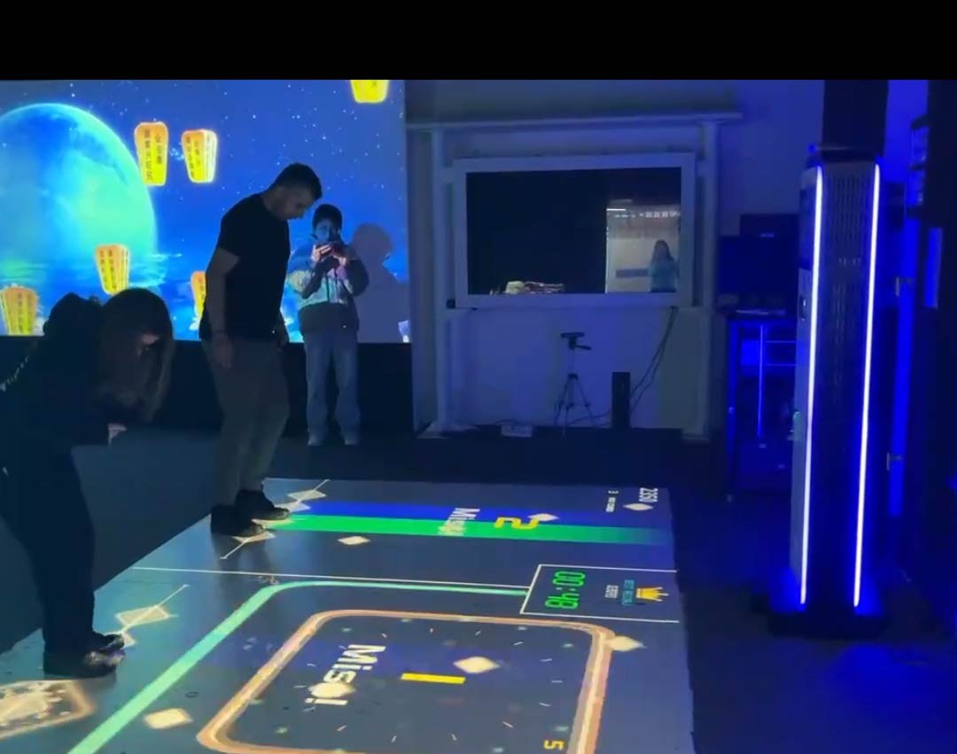 Video: family plays a glowing floor course while a moonlit lantern scene fills the wall behind them