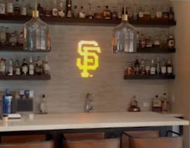 Video: yellow interlocking-letter monogram gobo lights a home bar wall lined with bottle shelves
