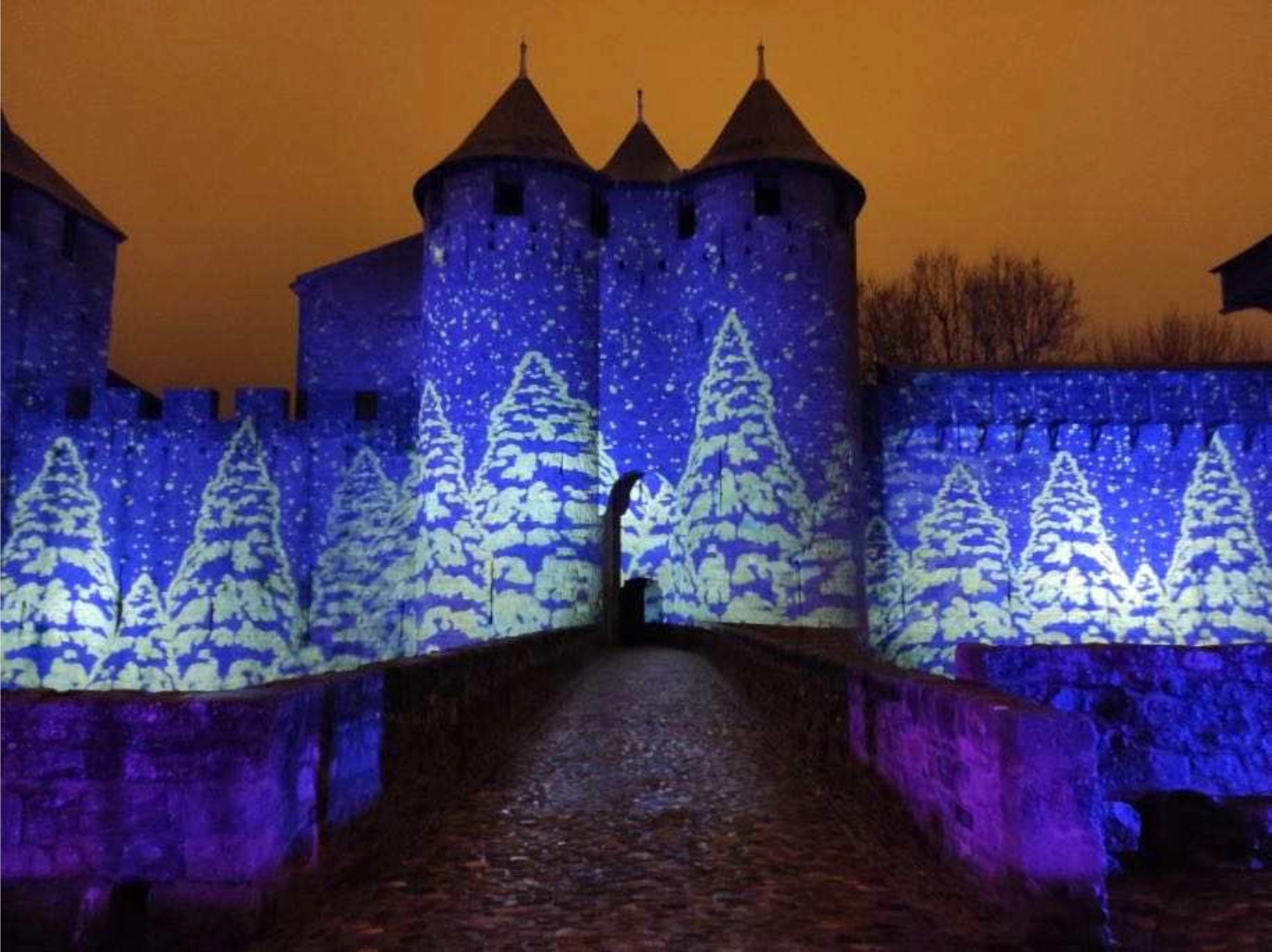 Snowy Christmas tree projections washing medieval castle towers and walls in blue winter light