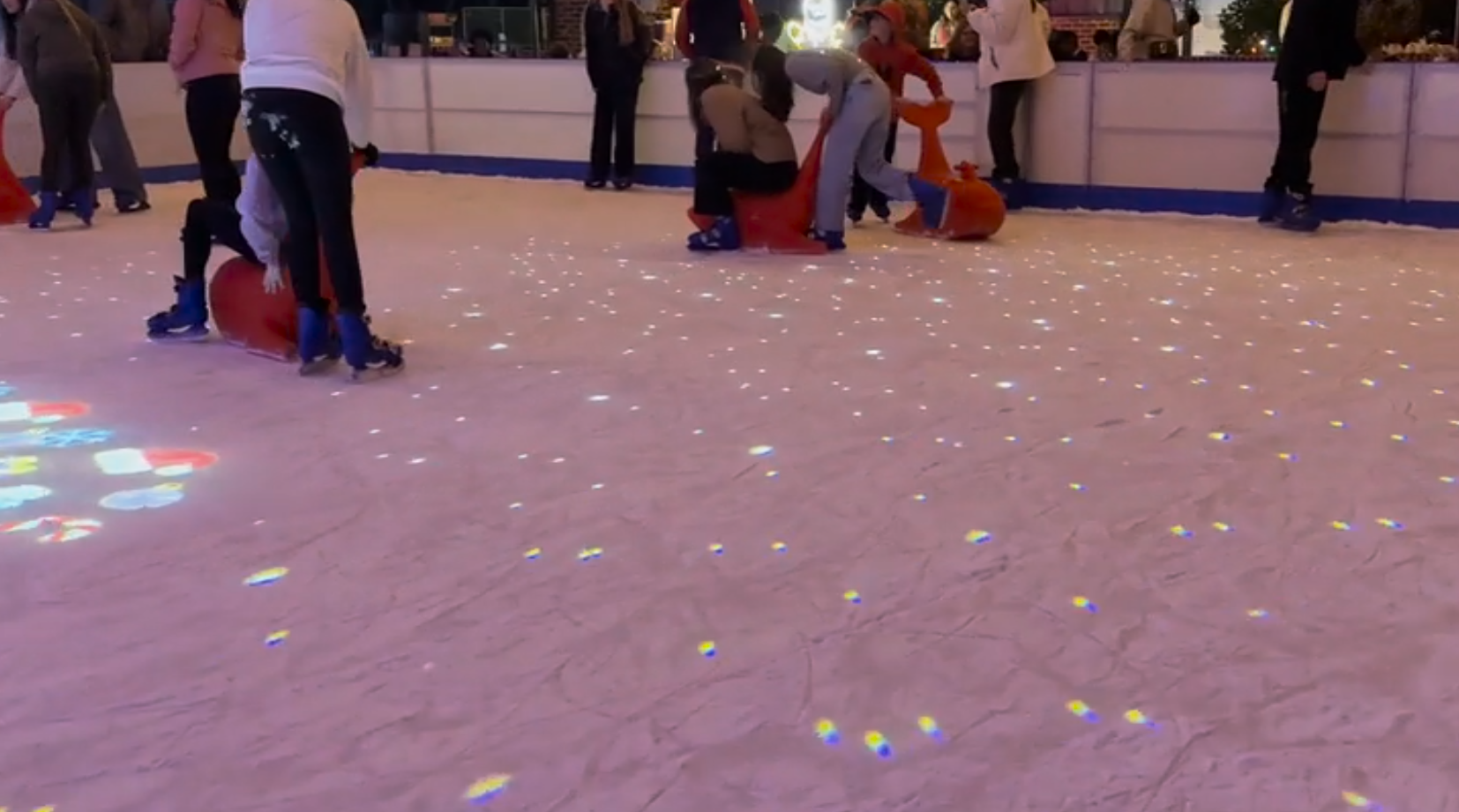 Video: colorful laser dots sparkle across a crowded ice rink as skaters glide at night