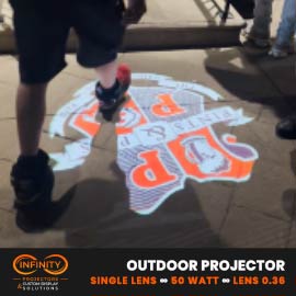 Video: orange restaurant crest gobo shines on a night sidewalk as pedestrians walk past