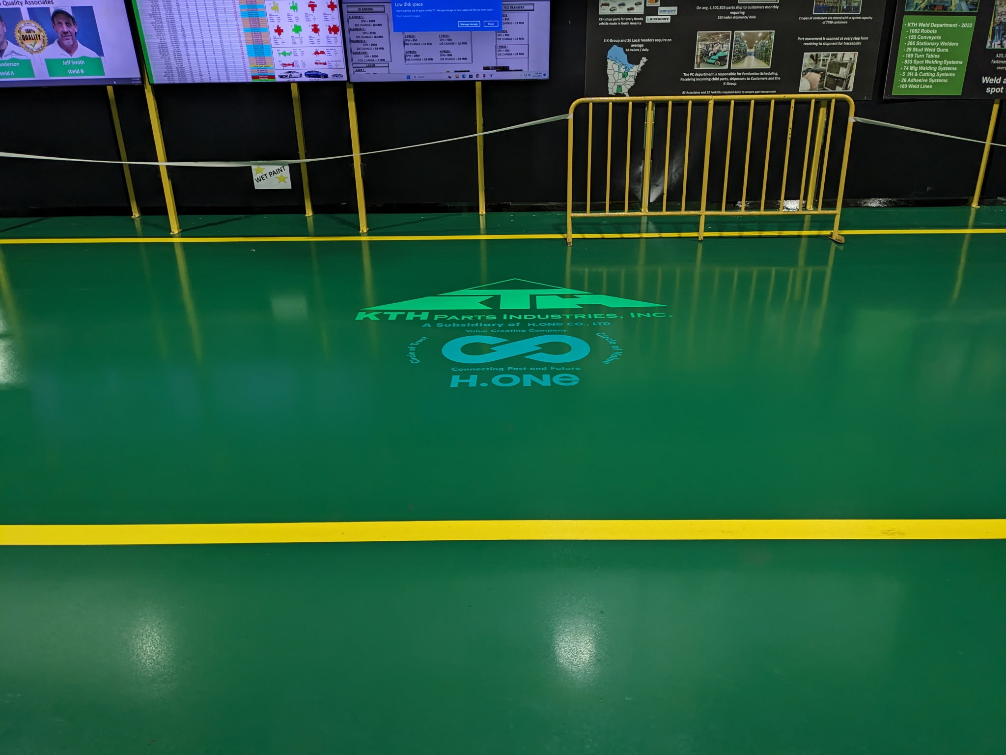 Safety floor projection on a warehouse and factory floor at KTH Parts Industries, an automotive-parts manufacturing facility, near storage racks and shipping containers — Infinity Projectors