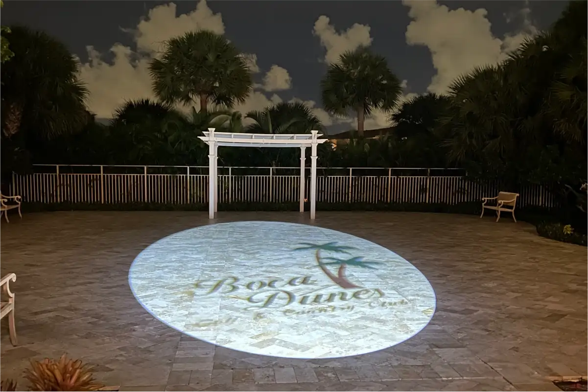 Boca Dunes Golf and Country Club logo projected on a paver patio at night in front of a white pergola