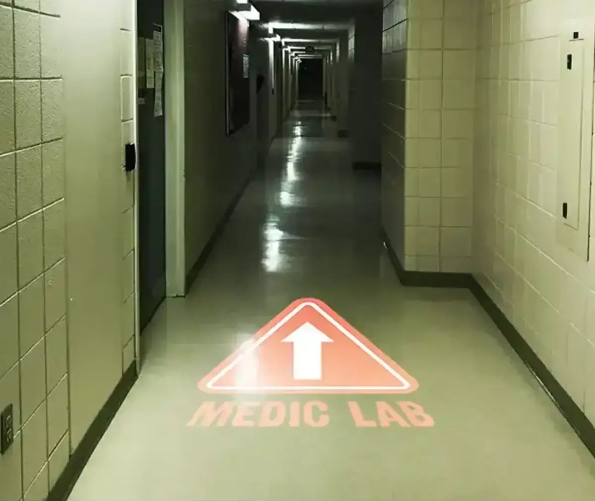 Red medic-lab arrow triangle projected on a clinic corridor floor, wayfinding after dark — Infinity Projectors