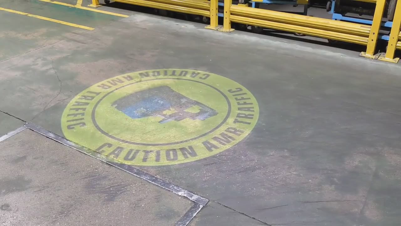 Rotating caution sign projected on a warehouse walkway next to guardrails — virtual safety signage projector — Infinity Projectors