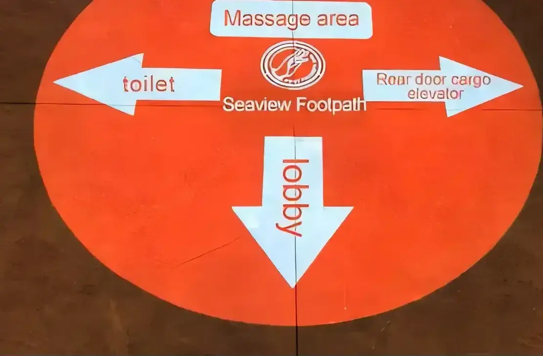 Orange wayfinding circle with arrows to lobby and massage area projected on a spa floor by a gobo projector — Infinity Projectors