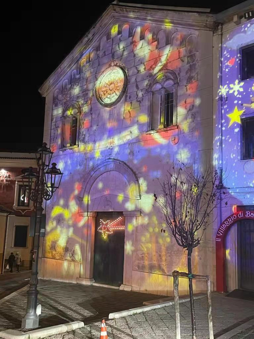 Colorful holiday stars and comets washing an old stone church facade at night from an outdoor projector — Infinity Projectors