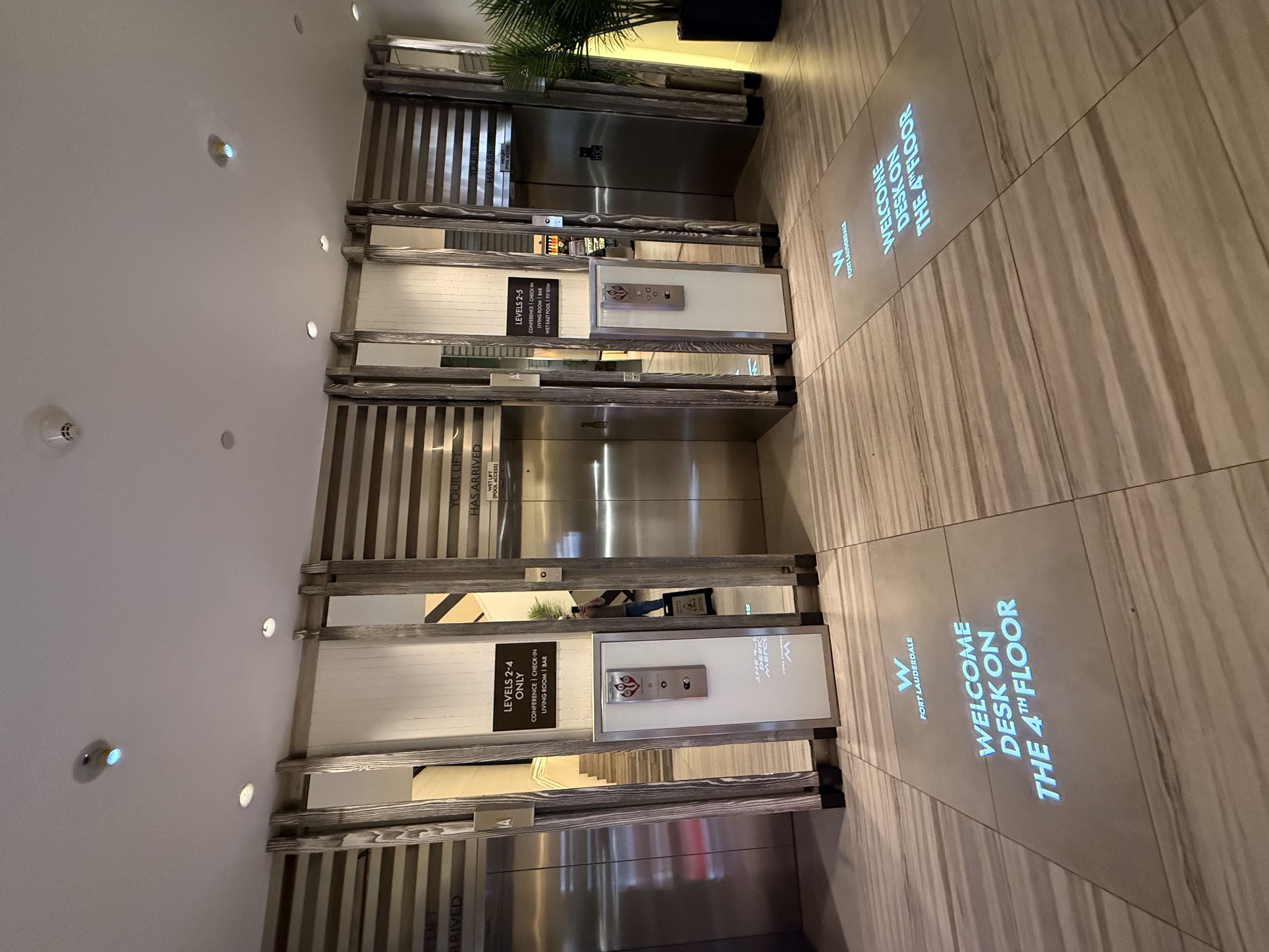 Two blue WELCOME DESK ON THE 4TH FLOOR floor projections in front of a hotel elevator bank — Infinity Projectors
