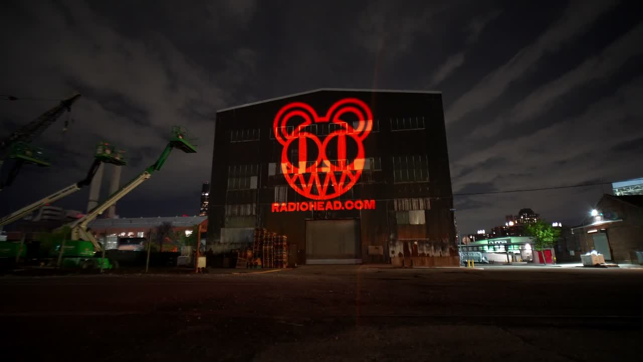 The same 1500W projector projecting a red bear-face logo with RADIOHEAD.COM across the building at night — Infinity Projectors