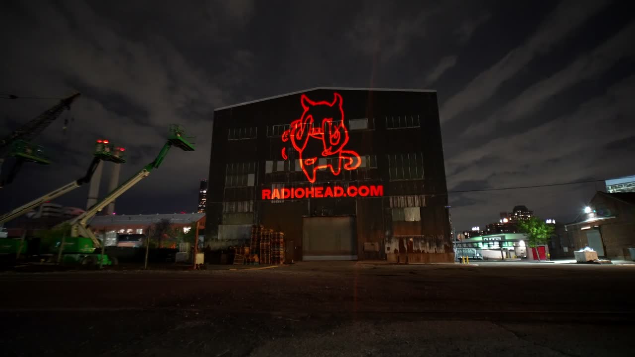 One of four designs from a single 1500W projector: a red creature outline with RADIOHEAD.COM projected across a building facade at night — Infinity Projectors