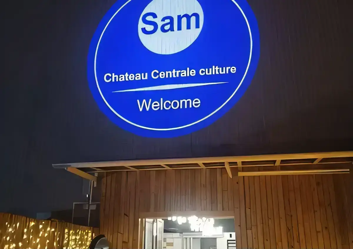 A venue's round blue Welcome greeting projected large on a dark wall above a timber-clad entrance after dark