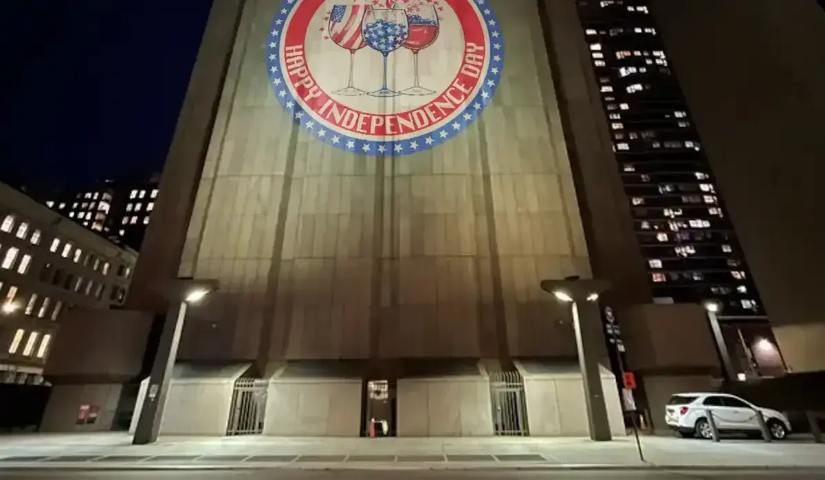 Patriotic Happy Independence Day seal with flag-themed wine glasses lighting up a concrete tower facade at night