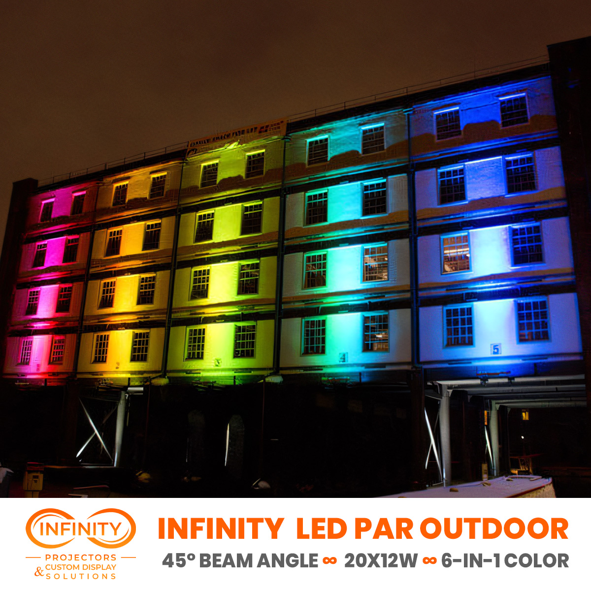 Five-story factory building with each bay lit a rainbow color, windows glowing pink to blue at night — Infinity Projectors