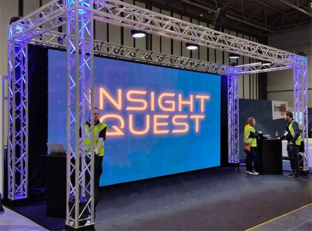 Large LED video wall in a truss frame showing bold orange text at an exhibition booth — Infinity Projectors