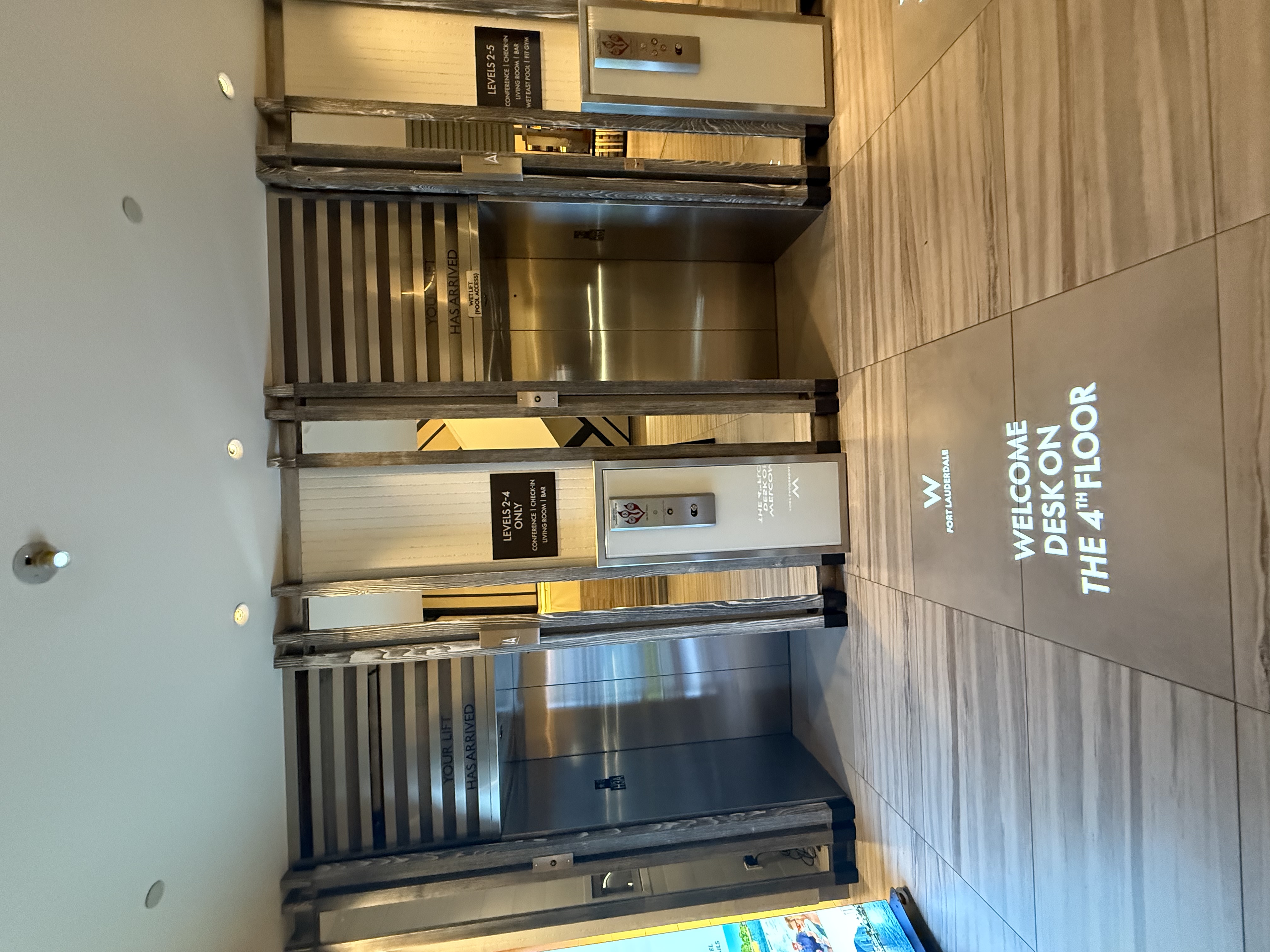 Hotel elevator lobby where a projected white sign reads Welcome Desk on the 4th Floor across the wood wall — Infinity Projectors