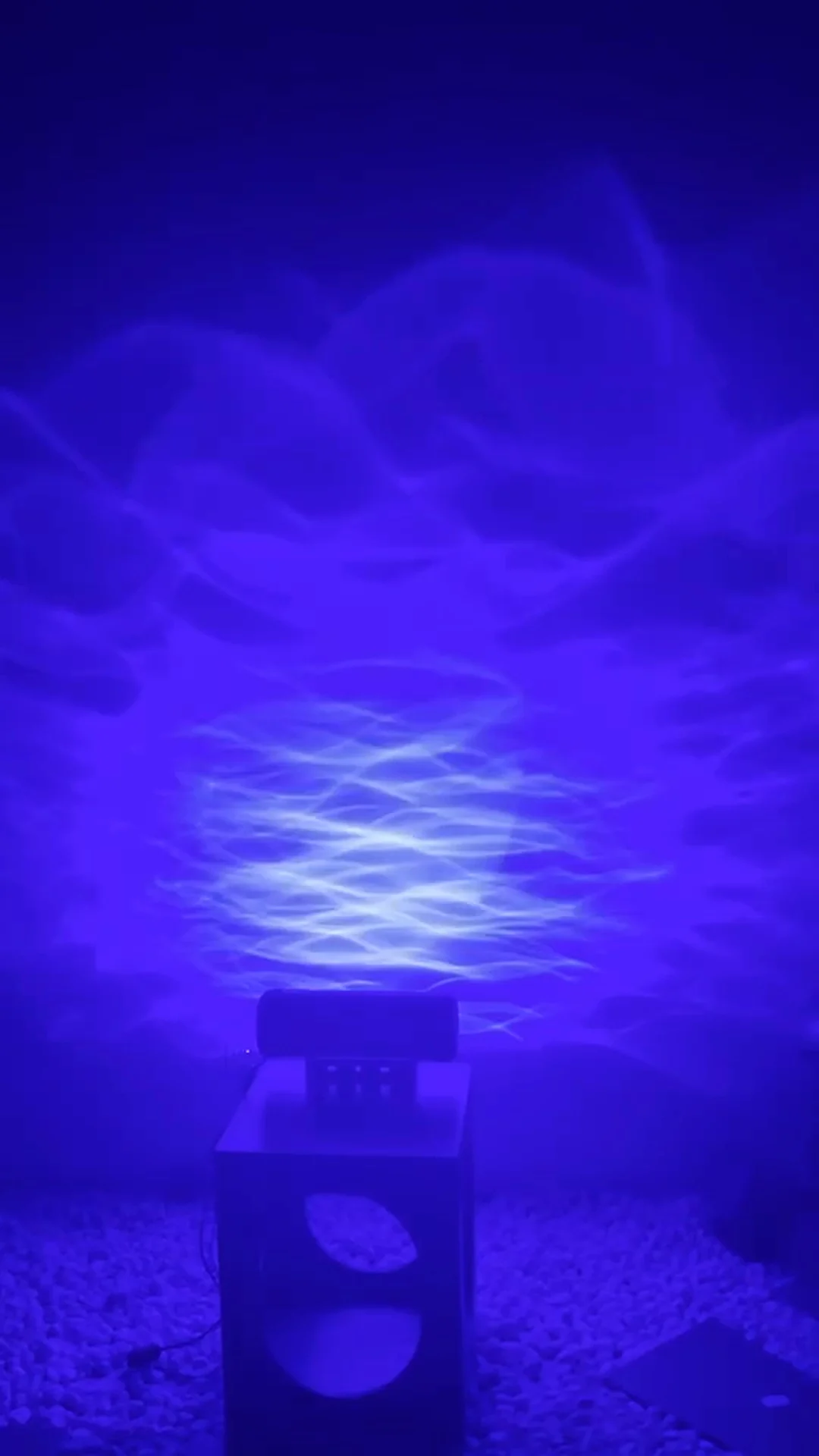 The Aurora on its stand, its window glowing as it throws blue waves up the wall — Infinity Projectors