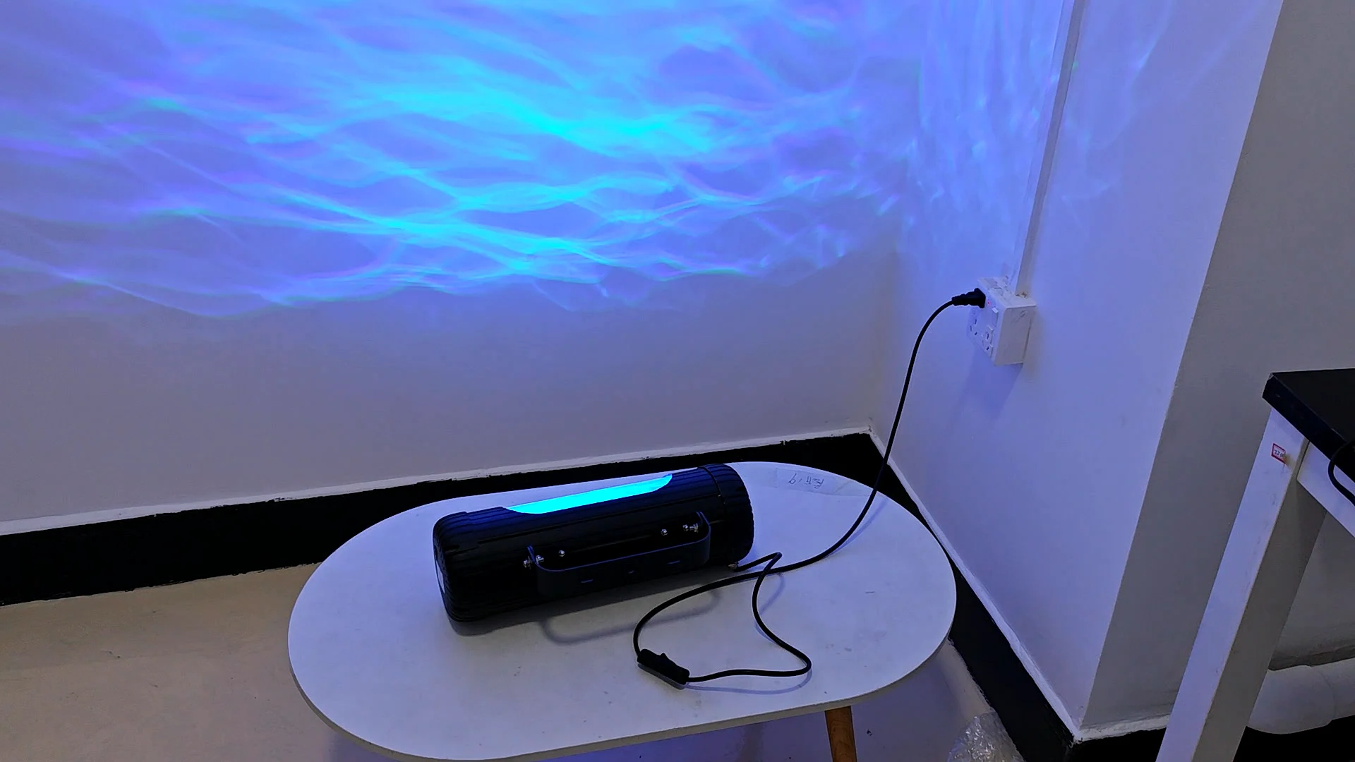 The Aurora Water Wave Projector on a side table, throwing blue waves across the wall — Infinity Projectors