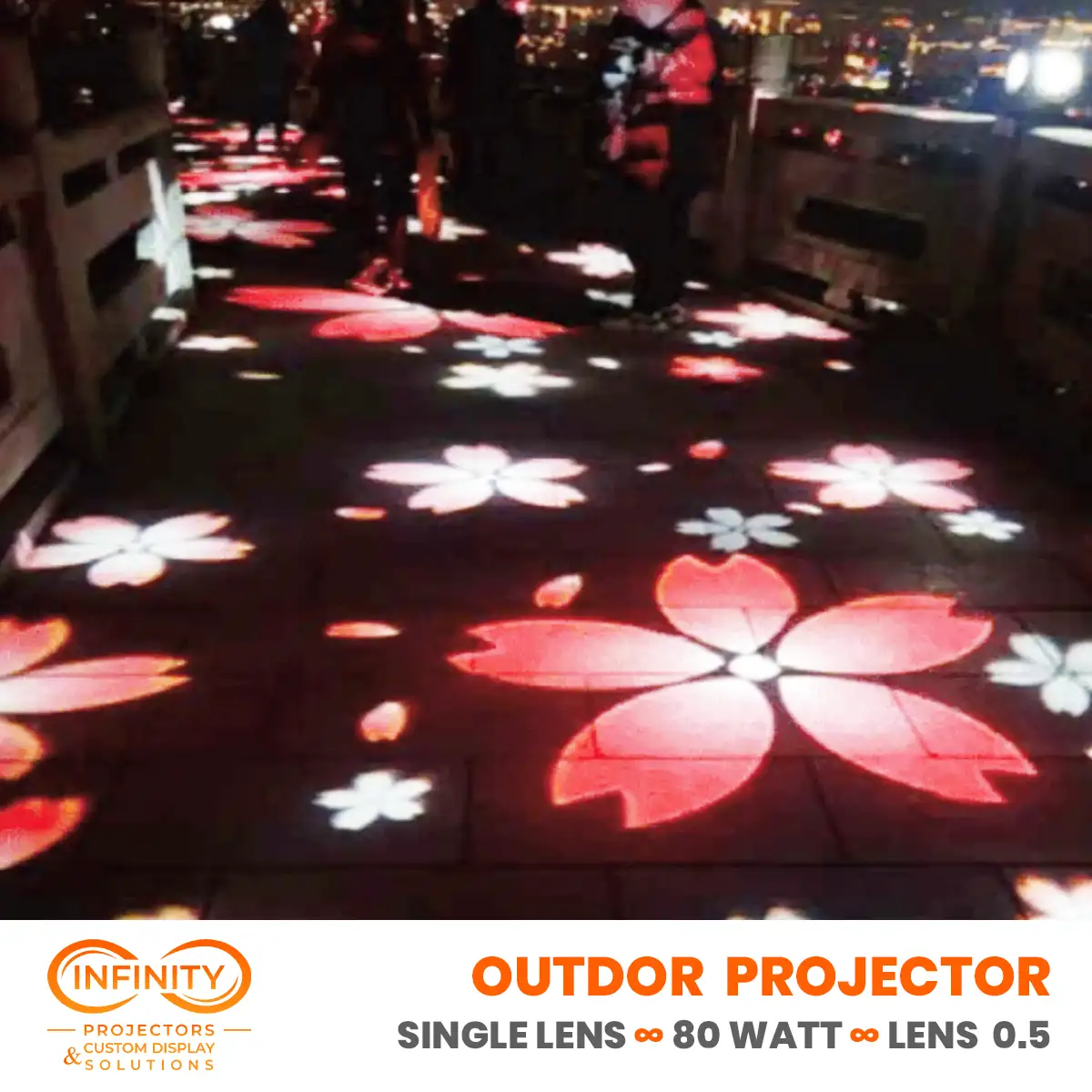 Pink and white cherry blossom gobos drifting across dark pavement as crowds stroll above city lights at night