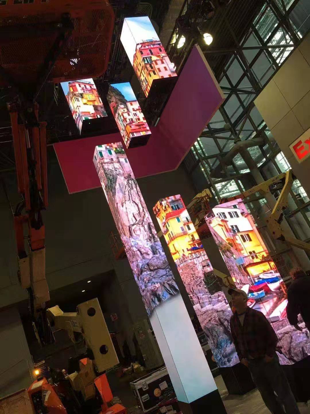 Crews installing tall LED pillar displays showing a colorful seaside village in a convention hall — Infinity Projectors