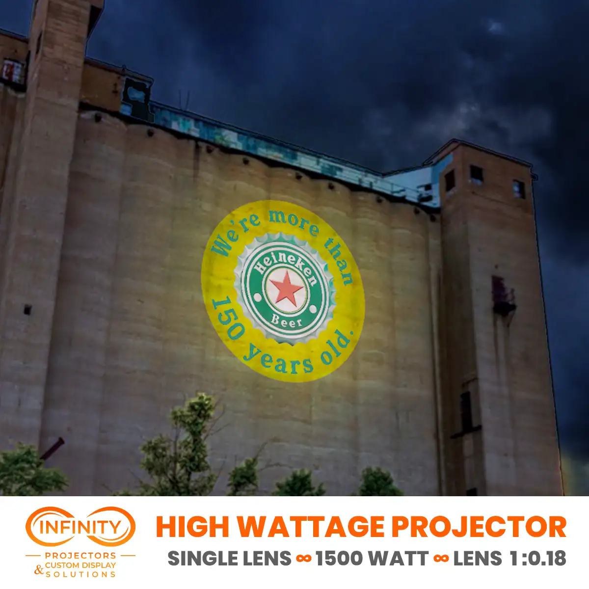 A beer brand's bottle-cap anniversary logo projected in yellow onto a massive concrete grain silo under stormy skies