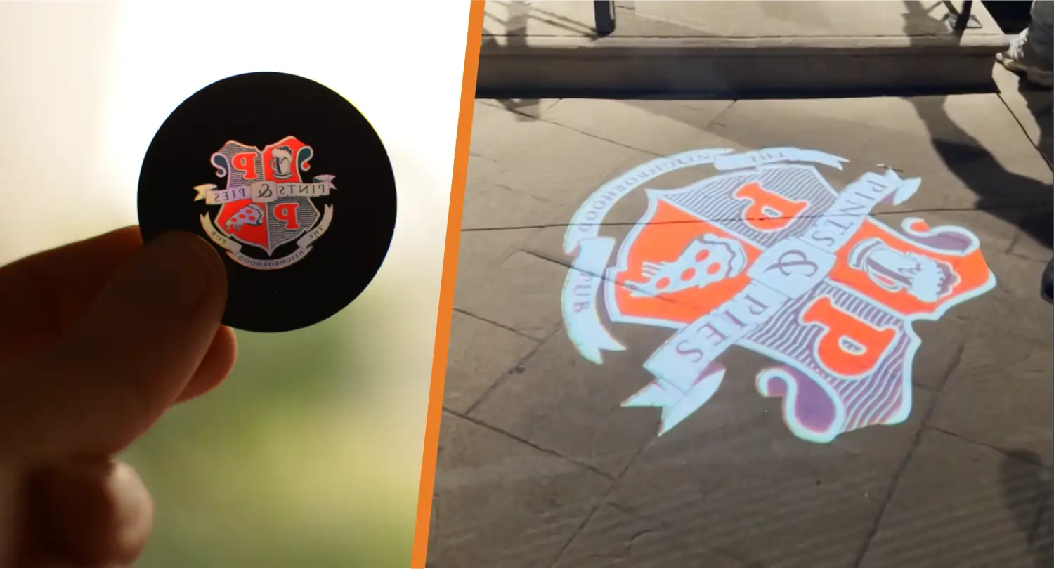 Fingers holding a full-color crest gobo next to the same design projected on stone pavers