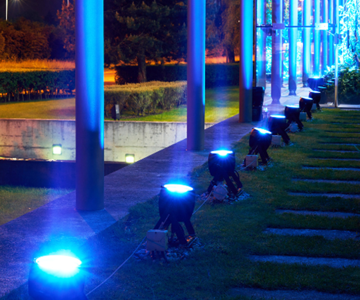 Blue landscape uplighting washing a modern building facade along a lit walkway and lawn — Infinity Projectors