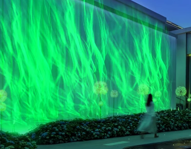Green aurora water wave light covering a long garden wall at night as a woman walks past — Infinity Projectors
