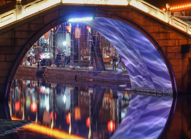 Aurora water wave effect projected under a stone bridge arch over a canal at night — Infinity Projectors