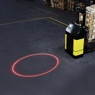 A red laser circle projected on a warehouse floor beside a yellow mobile robot — Infinity Projectors
