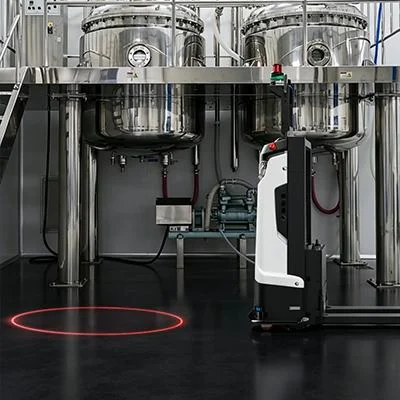 A red laser circle on the floor next to a mobile robot working between production tanks — Infinity Projectors