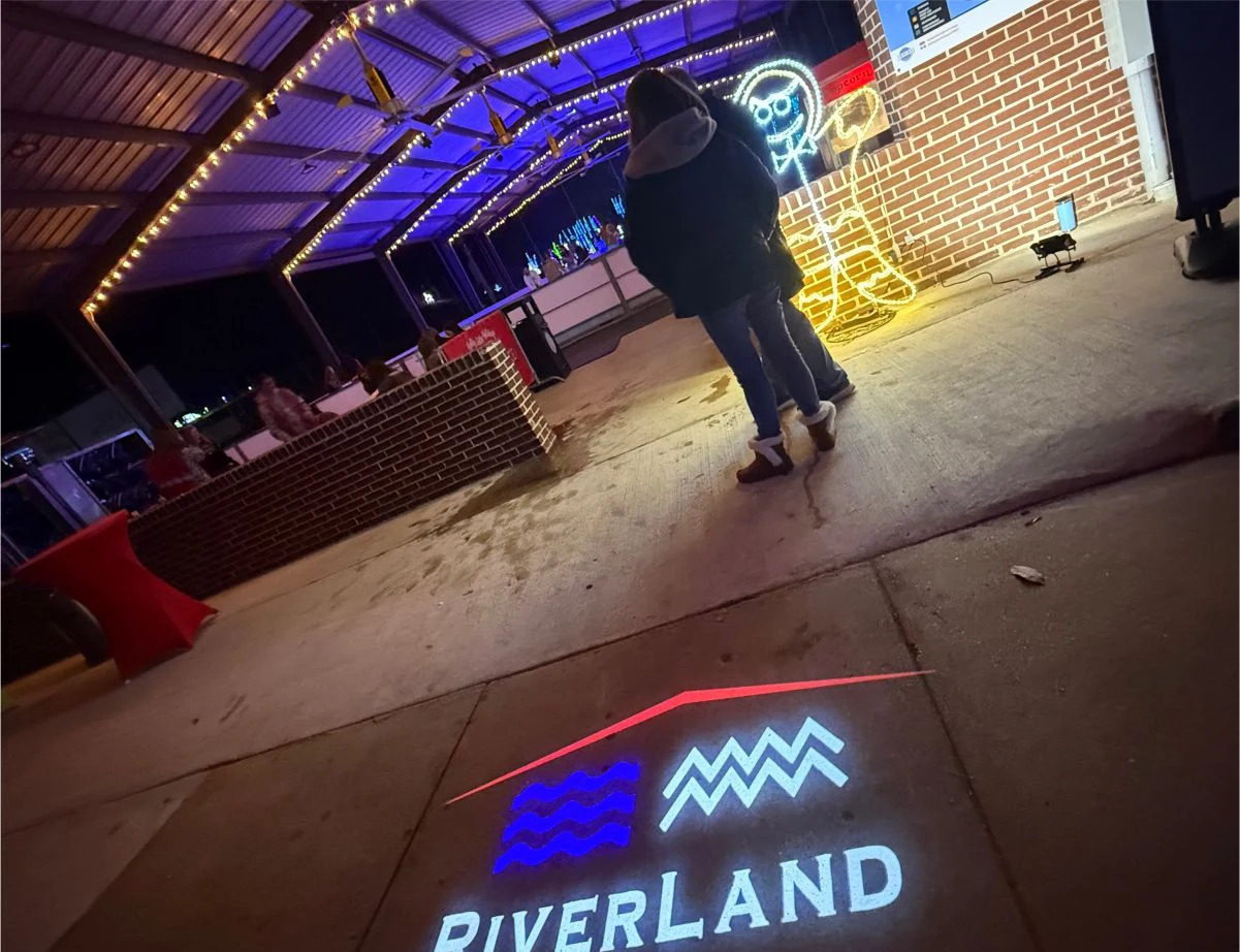 Venue logo with red roofline and wave marks projected on a concrete floor under string lights; product banner below