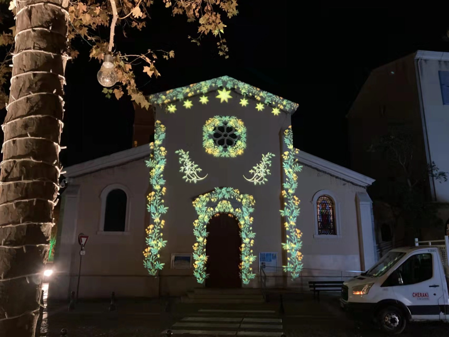 Floral gobo garlands and stars frame a chapel doorway and gable in green and gold light at night — Infinity Projectors