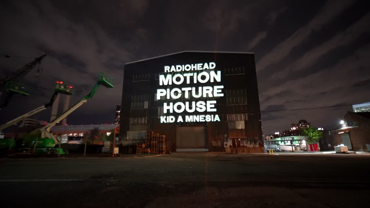 The same 1500W projector on the same wall, now projecting the white RADIOHEAD MOTION PICTURE HOUSE wordmark — Infinity Projectors
