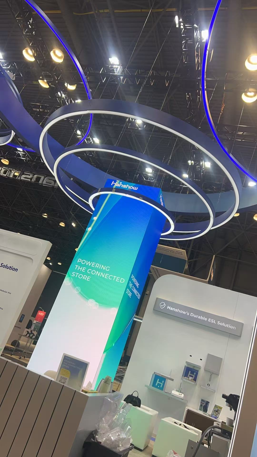 Curved LED column displaying retail messaging beneath giant ring lights at a trade show booth — Infinity Projectors