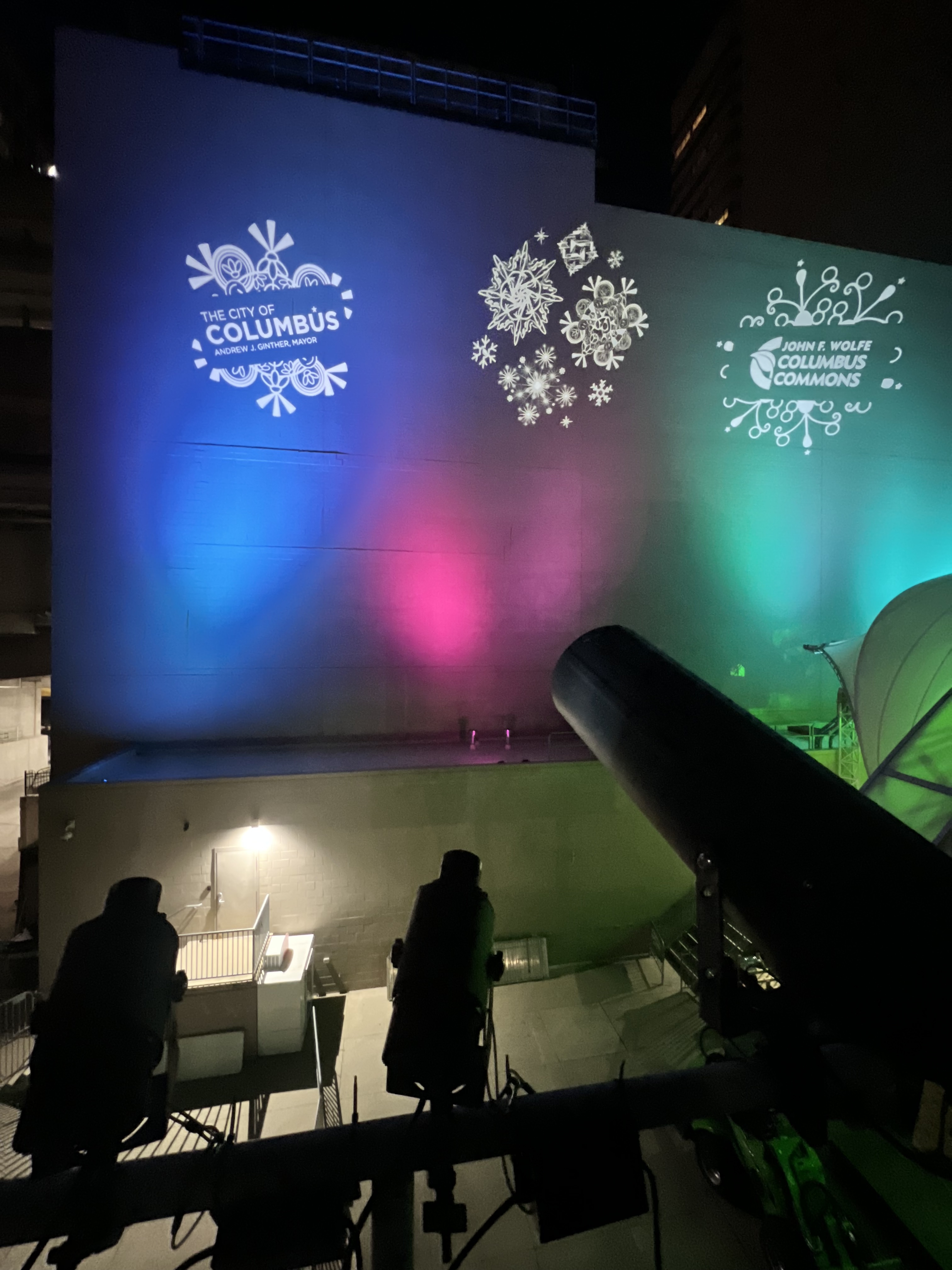 City of Columbus and Columbus Commons logos with snowflakes projected on a tall wall lit blue, pink and green