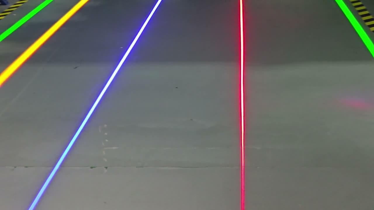 Green, yellow, blue, and red laser guide lines projected across a warehouse floor, locked-off shot for hero background use — Infinity Projectors