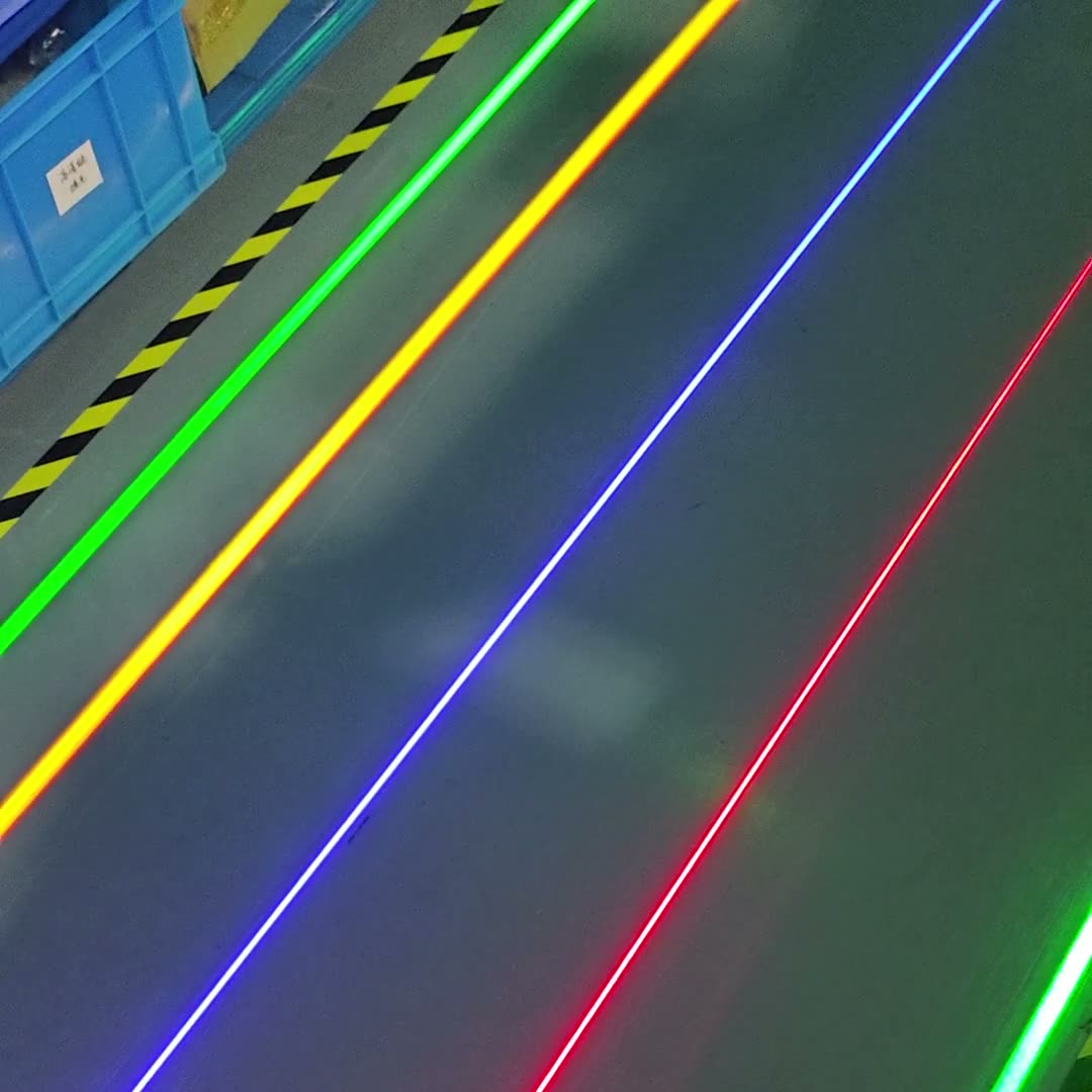 Laser line projector casting four simultaneous colored floor lines, green, yellow, blue, and red, in a warehouse aisle with hazard tape — Infinity Projectors