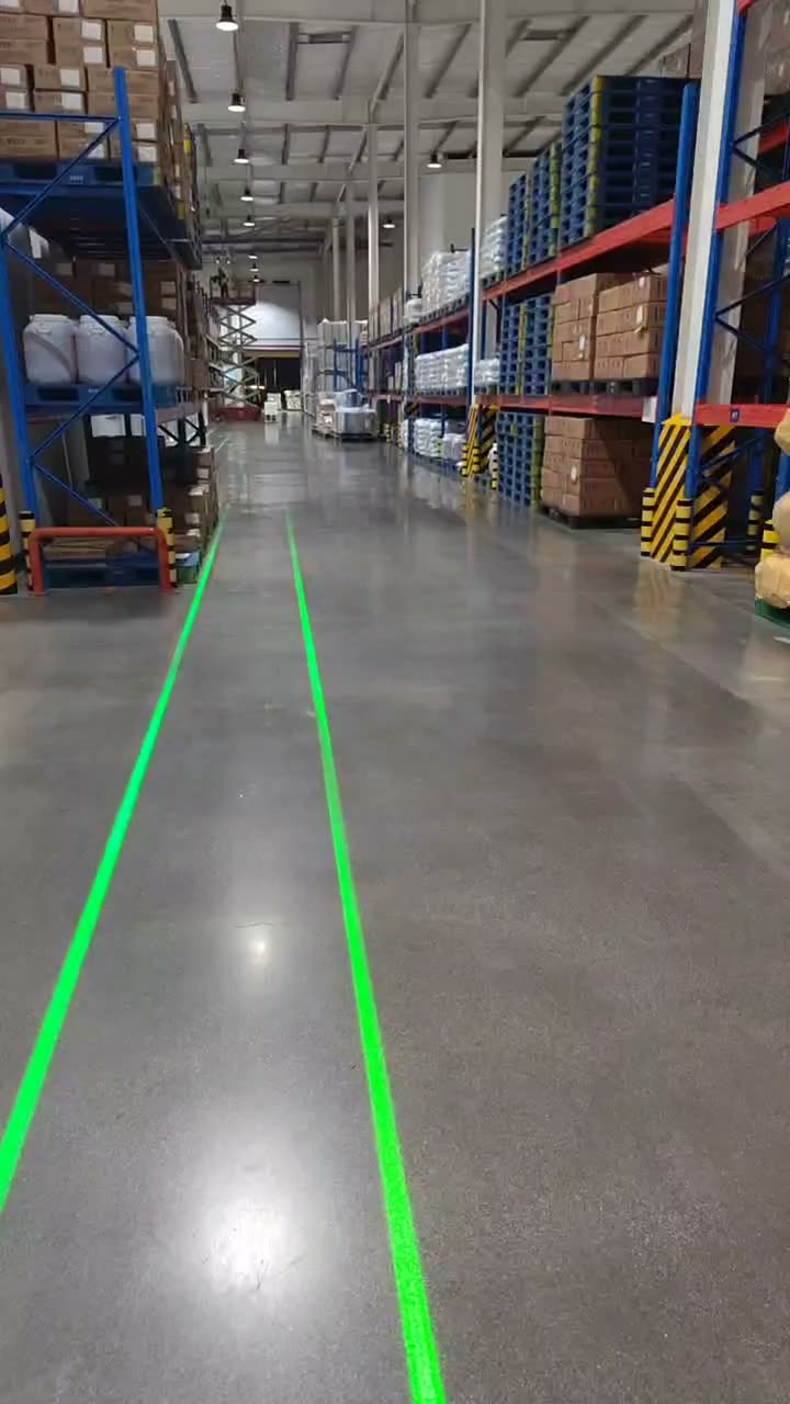 Dual green laser safety lines guiding down a tall pallet-racking warehouse aisle, camera walking the full length of the aisle — Infinity Projectors