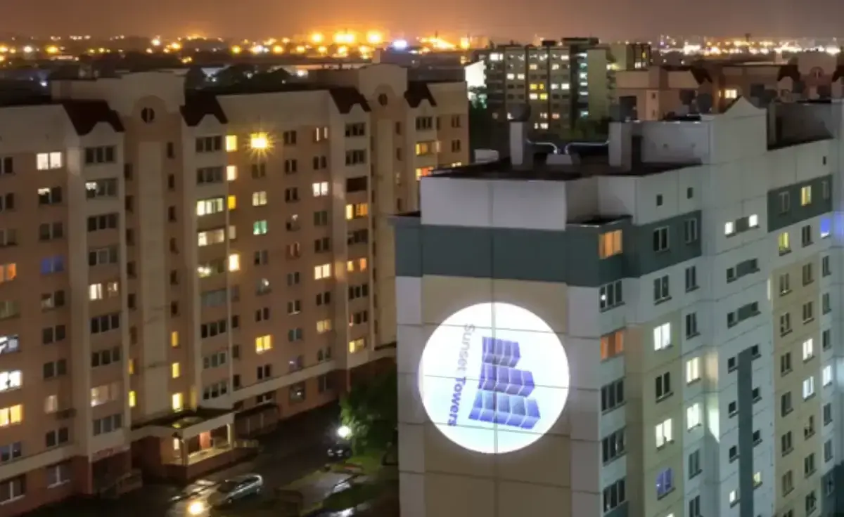 Apartment tower at night with a residence logo projected in a bright circle high on its facade — outdoor logo projector — Infinity Projectors